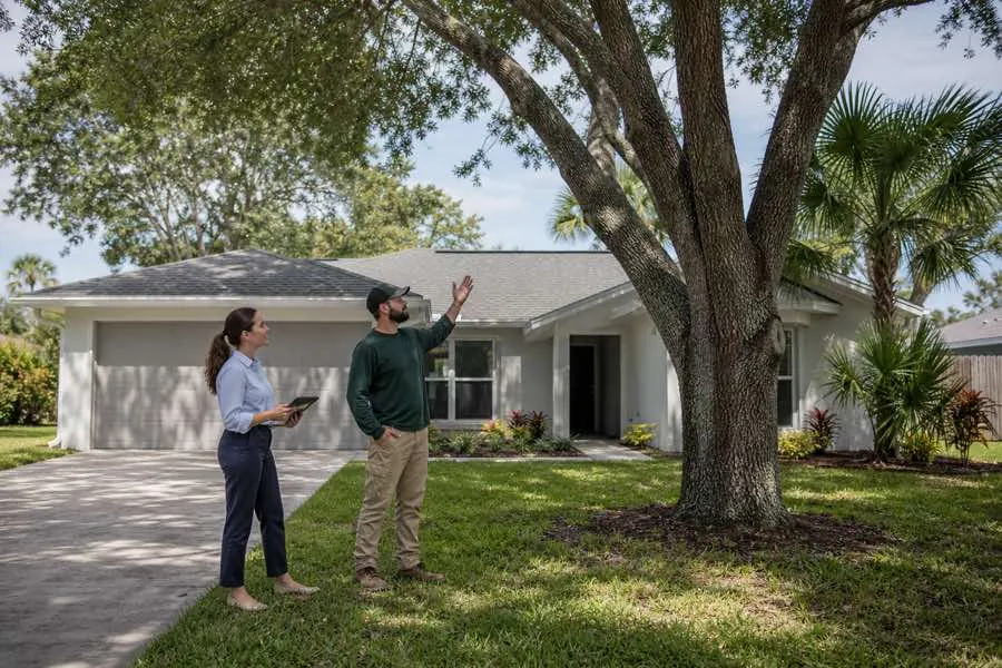 Two people beside a tree in front of a single-story house.