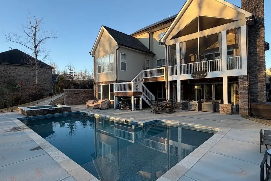 House Renovation and Outdoor Living Features Rear view of a large two-story house with a screened porch, raised deck, stone chimney, patio, and in-ground swimming pool
