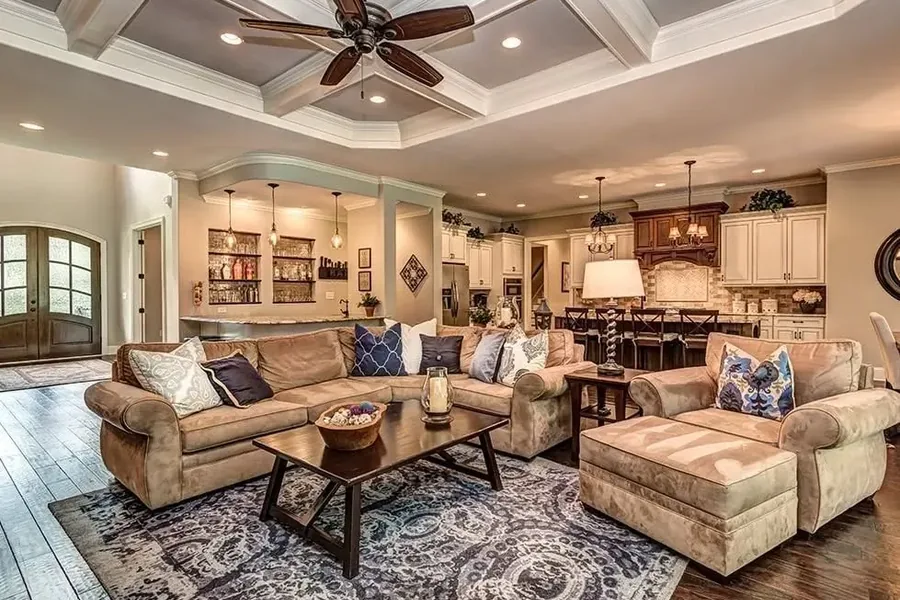 Open-Plan Interior for Rural Home Planning Spacious open-plan home interior with sectional seating, a patterned rug, coffee table, kitchen, dining area, and coffered ceiling with a fan