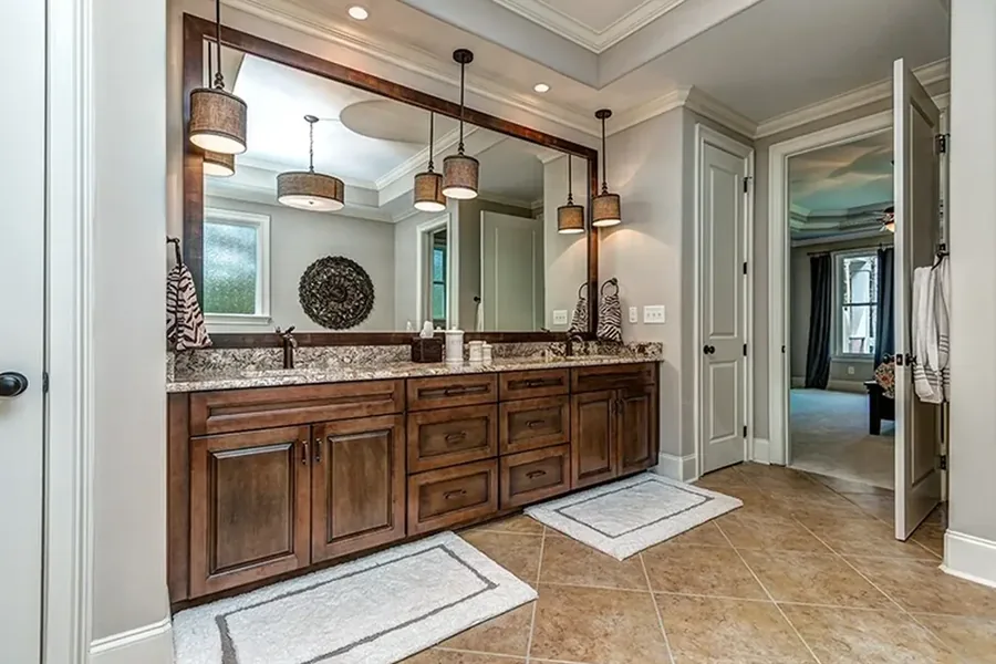 Spacious bathroom with a long double vanity, granite countertop, wood cabinetry, large framed mirror, pendant lights, and tiled floor